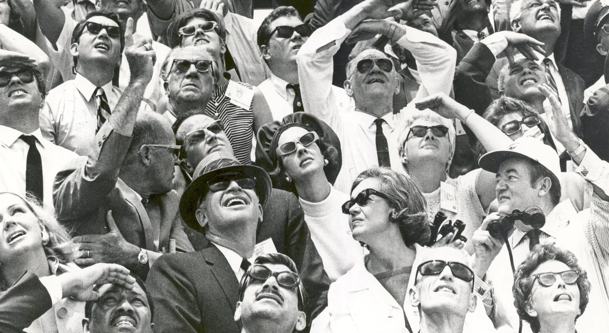 A crowd in sunglasses looking up at the sky